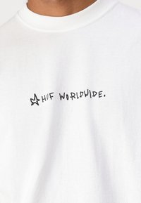 White cotton t-shirt featuring a black handwritten design with the text "HUF WORLDWIDE." Includes a star accent near the text.