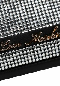Svart handväska med ett mönster av kristalldekorationer, med en gyllen "Love Moschino"-logotyp. Slät textur med en strukturerad form.
