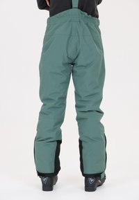 Vattentäta skidbyxor i grönt med justerbara hängslen. Har en svart accent vid nederkanterna och en avslappnad, baggy passform.