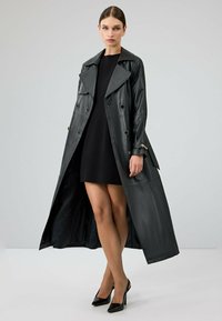 Zwarte leren trenchcoat met een dubbel-breasted ontwerp, grote revers en decoratieve knopen. Heeft een lange lengte met een open voorkant.