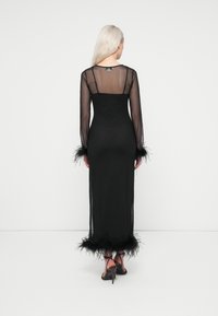 Vestido preto feito de material transparente com mangas longas e detalhes em penas nos punhos e na barra. Silhueta ajustada com decote nas costas.