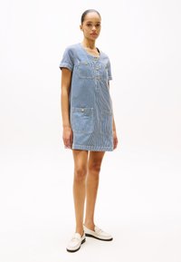 Rochie camisă cu dungi albastre și albe, având mâneci scurte, închidere cu butoane, două buzunare frontale și o croială lejeră, asortată cu loafers albi.