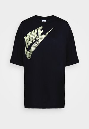 Čierne oversized tričko vyrobené z bavlny s veľkým perforovaným žltým logom Nike na prednej strane. Kruhový výstrih a krátke rukávy.