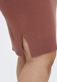 Gebreide rok in roestkleur met zijsplits aan de zoom. Heeft een zachte textuur en een getailleerd ontwerp, dat een gladde en lichte stof benadrukt.