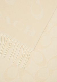 Kremo spalvos šalikas, pagamintas iš minkštos medžiagos, turintis subtilų logotipo raštą, baigtas subtiliais kutais viename krašte.