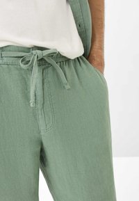 Light green, linen blend pants with a drawstring waist, front pockets, and a relaxed fit. Smooth texture, casual design.