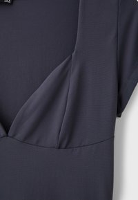 Tissu gris foncé avec un détail de couture froncée et une manche courte, montrant la texture et la structure de la partie supérieure d’un vêtement.