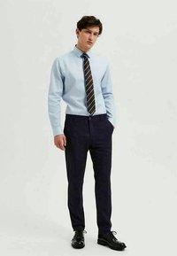 Light blue long-sleeve shirt, black and white striped tie, navy trousers, and black dress shoes, with a fitted design and smooth texture.