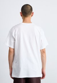 Tricou alb din bumbac cu o croială lejeră, mâneci scurte și gât rotund. Design minimalist fără logo-uri sau tipare vizibile.
