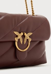 Χειροποίητη δερμάτινη τσάντα ώμου σε μπορντό χρώμα με ραμμένο σχέδιο, μεταλλικά διακοσμητικά σε σχήμα πουλιού σε χρυσό τόνο και πλεκτό αλυσίδα ιμάντα. Διαθέτει μαγνητικό κούμπωμα.