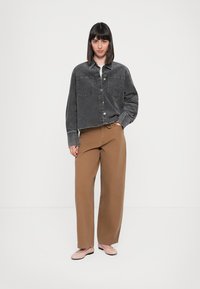 Grå cropped denimjakke med knaplukning og to brystlommer, parret med brune vidde bukser og flade rosa sko.