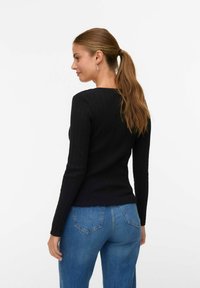 Top nero a maniche lunghe con costine e scollatura rotonda, abbinato a jeans in denim blu a vita alta. L'outfit presenta una silhouette aderente.