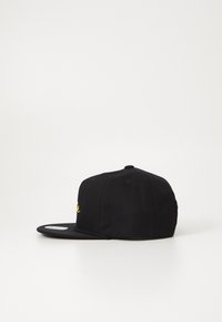 Svart caps med flat skygge, med en gul brodert logo på framsiden, laget av stoff med en glatt tekstur.