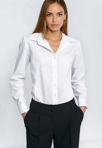 Biała koszula na guziki z kołnierzykiem, z długimi rękawami, wykonana z gładkiego materiału; zestawiona z czarnymi, wysokim stanem spodniami z bocznymi kieszeniami.