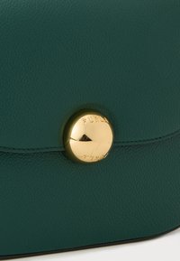 Borsa a tracolla in pelle verde acqua caratterizzata da un prominente chiusura circolare dorata con incisione "FURLA", texture liscia e dettagli di cucitura discreti.