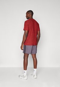 Red short-sleeved athletic shirt with a textured pattern, paired with gray shorts featuring three black stripes, and white socks with logo.