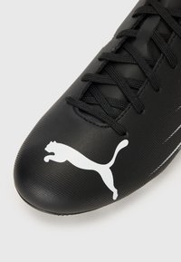 Crne nogometne kopačke s teksturiranim sintetičkim gornjim dijelom, ravnim vezicama i istaknutim bijelim Puma logotipom sa strane.