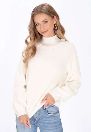 Crème-kleurige trui met een hoge kraag, geribbelde structuur en uitgerafelde mouwen. Gecombineerd met lichtblauwe jeans met een relaxte pasvorm.