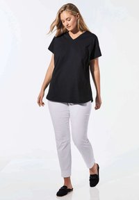 Schwarzes V-Ausschnitt-T-Shirt mit kurzen Ärmeln, kombiniert mit hellgrauen Hosen und schwarzen Slippern. Einfaches Design, lockere Passform, glattes Material.