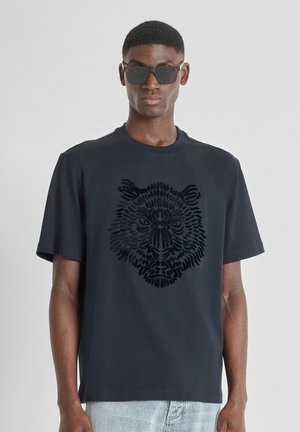 T-shirt navy a maniche corte con una grafica in rilievo di una testa di leone nera. Realizzato in cotone morbido, con design a girocollo e vestibilità rilassata.