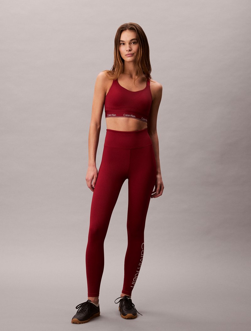 Burgundi värvi sportbra ja retuuside komplekt, mis on valmistatud venivast kangast; funktsioonid Calvin Kleini logo bändil ja retuuside külgedel. Mustad spordijalatsid.