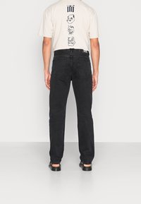 Schwarze gerade Jeans mit hoher Taille, aus Denimstoff, mit sichtbaren Gesäßtaschen und einem schlichten Design, kombiniert mit einem beigen T-Shirt mit Grafikdruck.