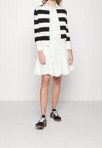 Czarny i biały kardigan w paski na białej sukience z wiązaniem w talii, zestawiony z czarno-białymi sneakersami. Gładki materiał, luźny krój.