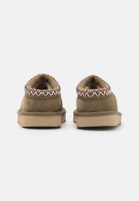 Bruna mockaskinn slip-on skor med en tan gummisula, med en dekorativ vävd accent längs kragen. Mjuk innerfoder synlig.