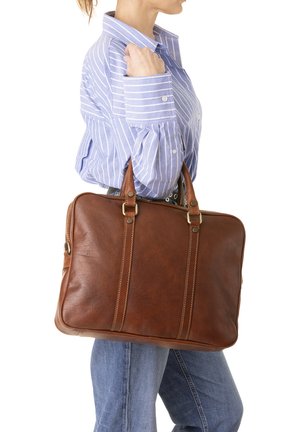 Valigetta in pelle marrone con manici doppi, caratterizzata da una superficie liscia e due linee di cucitura verticali. Indossata con una camicia a righe blu.