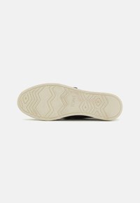 Schwarze Sneaker mit einer weißen Gummisohle, die ein Zickzackprofil aufweist. Textil-Obermaterial mit minimalen Branding-Details.