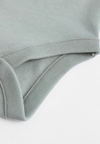 Tessuto di cotone verde chiaro con una texture liscia, dotato di un collo rotondo e bordi cuciti, che mostra flessibilità e comfort.