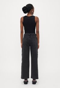 Top preto sem mangas combinado com jeans cargo de cintura alta e perna larga em denim escuro, com dois bolsos laterais e acabamento limpo. Sapatos pretos completam o visual.