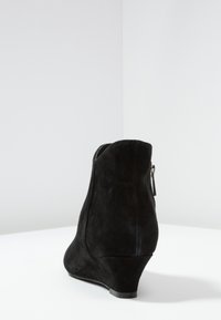 Bottines à talon en suède noir avec un bout arrondi, une fermeture éclair sur le côté et une finition texturée. Le talon compensé est légèrement courbé et lisse.