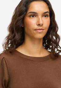 Pull en tricot marron avec un col rond et des manches courtes légèrement froncées. La texture semble douce et lisse.