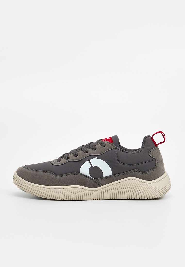 Zapatilla gris con una textura suave, con un gran logo azul claro, detalles rojos en el talón y una suela gruesa de goma blanca.