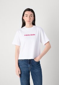 Balds kokvilnas T-krekls ar īsām piedurknēm, kuram uz krūšu ir rozā izšūts "Calvin Klein" logo un kuram ir brīvs piegriezums.
