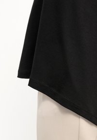 T-shirt nera in cotone con orlo curvo e maniche corte, che mostra una consistenza morbida e un design semplice, abbinata a pantaloni chiari.