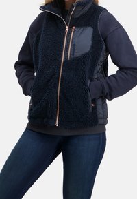 Marinfärgad fleeceväst med dragkedja fram, med en texturerad ovandel och slät nederdel. Kopparfärgad hardware och sidofickor.