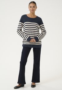 Jūras spēku svītrains garām piedurknēm džemperis ar krēmkrāsas svītrām, apaļu kakla izgriezumu un ribotām odziņām, apvienots ar tumšiem džinsa platām biksēm un melniem dzīvokļiem.