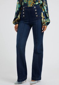 Høj talje denim jeans i mørkeblå, med en tætsiddende talje, brede ben og flere metalliske knapdetaljer på forsiden.