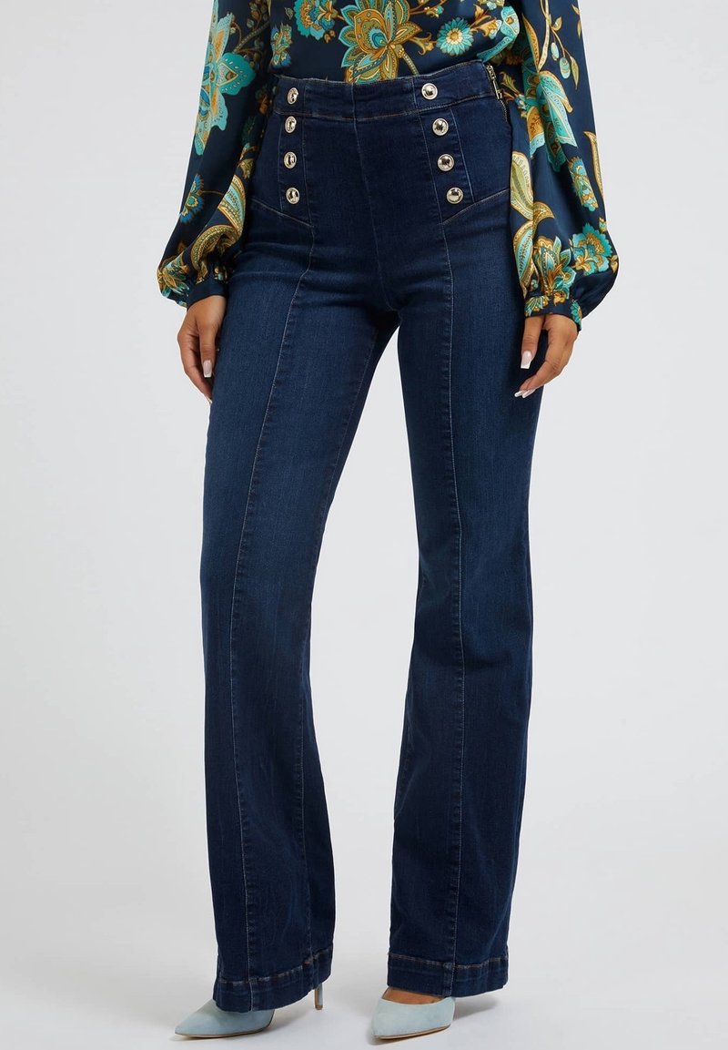 Jeans in denim a vita alta di colore blu scuro, con vita aderente, gambe larghe e numerosi accenti di bottoni metallici lungo la parte anteriore.