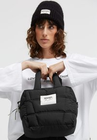 Schwarze gesteppte Stepphandtasche mit einem Steppmuster, zwei kurzen Griffen und einem Logo-Patch. Verfügt über eine Reißverschlusstasche und einen verstellbaren Riemen.