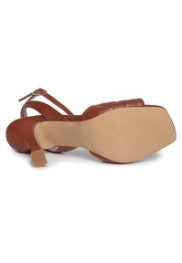 Sandalo con tacco alto in pelle marrone, dotato di una fascia trapuntata, fibbia regolabile alla caviglia e suola in gomma beige liscia.