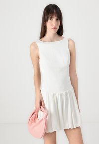 Rochie albă fără mâneci, cu un corset ajustat și o fustă evazată. Modelul tine în mână o geantă moale de culoare roz pal, cu un mâner legat. Design simplu, textură netedă.
