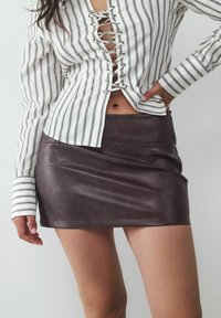 Wit en zwart gestreepte blouse met vetersluiting aan de voorkant en lange mouwen, gecombineerd met een strakke bruine neplederen minirok.