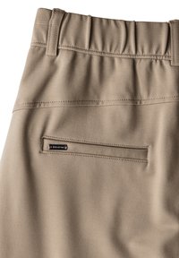 Beige broek met een elastische tailleband heeft een achterzak met een merklabel. Glad, stretchy stof met subtiele naden.