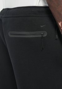 Crne Nike trenirke s patentnim zatvaračem i elastičnim pojasom. Glatka tekstura sa suptilnim logotipom na tkanini.