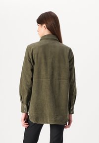 Camisa de corduroy verde-oliva com colarinho, mangas longas e punhos abotoados, com um padrão texturado e estriado e um fundo reto.