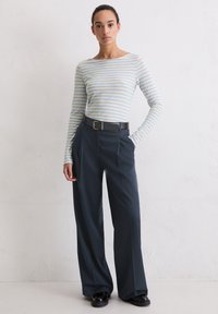 Gestreept shirt met lange mouwen in lichtblauw en wit, gecombineerd met donkerblauwe wijde broekspijpen, voorzien van een zwarte riem met een gouden gesp.