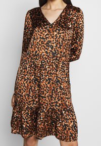 Leopardmönstrad klänning med V-ringning, långa ärmar, skikten på kjolen, i nyanser av brunt och svart. Slät textur; strukturerad design.